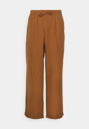 Brown linen pants with a loose fit, elastic waistband, drawstring tie, and two front pleats for added texture. Rolled cuffs at the hem.