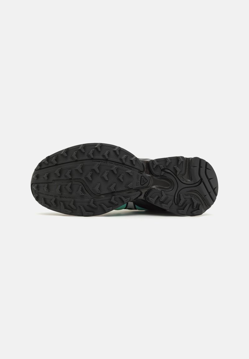 Suela de goma negra con un patrón de textura y acentos verdes. Cuenta con ranuras flexibles para tracción y soporte. Construcción duradera.