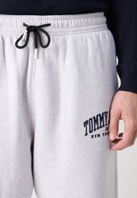 Světlé šedé tepláky s elastickým pasem, černým šňůrkovým stahováním a vyšívaným logem "TOMMY HILFIGER" v navy modré na stehně.