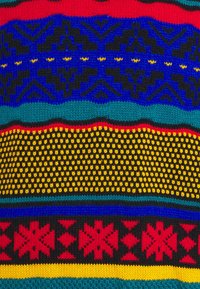 Tissu tricoté avec des motifs géométriques colorés, comprenant des étoiles rouges, des points jaunes, des formes noires et bleues sur des rayures vertes et rouges.