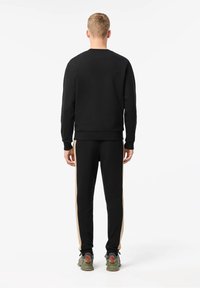 Černá mikina s dlouhými rukávy, žebrovanými manžetami a lemem. Kombinována s černými kalhotami s béžovými pruhy po stranách. Nositelná se šedými teniskami.