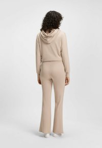 Beige hoodie en bijpassende flared pants, gemaakt van zacht materiaal, met een capuchon en elastische tailleband, weergegeven vanuit de achterkant.