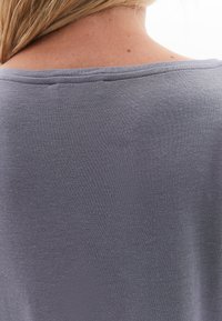 Grå kortärmad skjorta med mjuk textur och vid halsringning. Har en subtil lyster och slätt tyg utan mönster eller utsmyckningar.