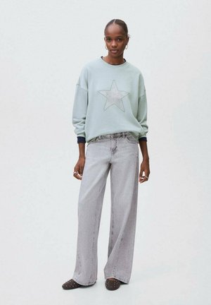 Ljusblå sweatshirt med stjärnmönster, kombinerad med höga grå vida jeans. Outfiten har en avslappnad passform och en casual stil.