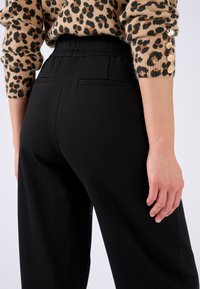 Pantalones negros de cintura alta con una textura suave y bolsillos traseros, combinados con un suéter estampado que presenta manchas de leopardo en beige y negro.