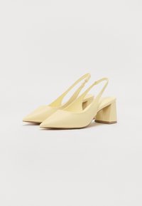 Kermakasta slingback-kengät, joissa on terävät varpaat ja lohkarekengät, lepäävät valkoisella pinnalla.