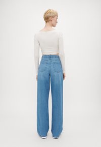 Λευκό cropped μπλουζάκι με μακριά μανίκια, συνδυασμένο με ψηλόμεσα, φαρδιά μπλε τζιν, που διαθέτουν δύο πίσω τσέπες και χαλαρή εφαρμογή.