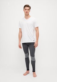 Fehér v nyakú póló sötétszürke leggings-szel, textúrával díszítve és testhezálló szabással, amely sportos viseletnek megfelelő.