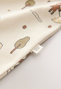 Tissu en coton avec un fond crème clair orné de motifs ludiques d'arbres, de feuilles et d'un ours tenant un parapluie, portant l'inscription "HELLO BEAR".