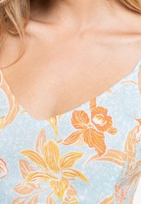 Robe à motif floral avec un fond bleu clair. Le design comprend des fleurs orange et jaunes avec une finition texturée et un décolleté en V.