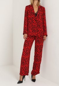 Czerwony garnitur w panterkę z długimi rękawami i głębokim dekoltem w kształcie litery V. Dopasowany krój, szerokie spodnie, w połączeniu z czarnymi szpilkami.