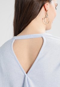 Haut en maille bleu clair avec une petite découpe au dos, col rond et texture douce. Ourlet arrondi et détail torsadé subtil.