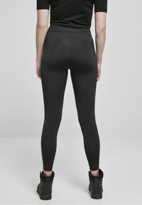 Černé legíny s vysokým pasem a hladkou texturou. Přiléhavý střih sahá ke kotníkům. V kombinaci s černými botami až ke kotníkům.