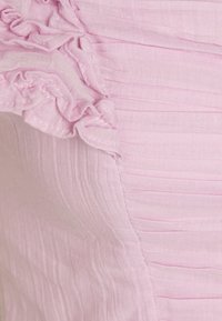 Ljust rosa tyg med vertikala veck och krusiga kanter, med en mjuk textur. Sömmar synliga längs sömmarna.