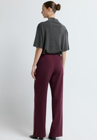 Szary sweter z dzianiny o luźnym kroju i krótkich rękawach, zestawiony z wysokim stanem burgundowymi spodniami, mającymi smukłą sylwetkę i boczną kieszeń.