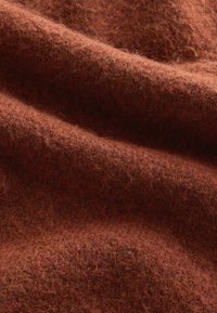 Tissu en laine doux et texturé de couleur rouille avec des fibres visibles et des plis doux qui créent une apparence chaleureuse et conviviale.