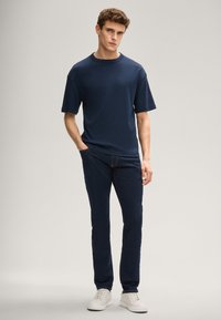 Granatowy t-shirt z krótkim rękawem, zestawiony z ciemnymi dżinsami, noszony z białymi tenisówkami. Materiał ma gładką fakturę, a krój jest luźny.