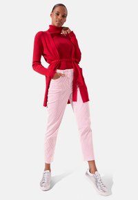 Rode geribbelde coltrui met een gestrikte taille, gecombineerd met lichtroze corduroy broek met streepjes en zilveren sneakers.