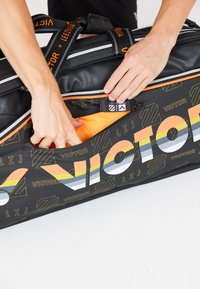 Sort duffelbag med orange detaljer, der har et stort "VICTOR" print. Den åbne lomme afslører et lyseorange interiør. Holdbart materiale.