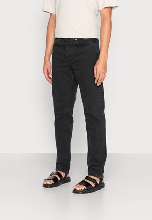 Vaqueros de mezclilla negra con un corte recto, combinados con una camiseta beige clara y sandalias negras. Diseño simple, sin patrones o acentos visibles.