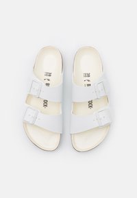 Witte sandalen met twee verstelbare gespen, vlak ontwerp, zachte voetbed en een natuurlijke beigem kleurige zool. Maat binnenin gedrukt, gladde textuur.