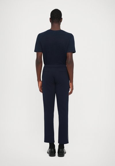 Navy T-Shirt mit kurzen Ärmeln, kombiniert mit navyfarbigen Hosen im geraden Schnitt und dezenten seitlichen Details, getragen mit schwarzen Schuhen.