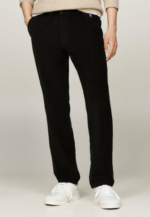 Pantalons en velours côtelé noir à coupe slim, avec des poches latérales et un petit logo à l'avant. Associés à des baskets blanches pour un contraste.