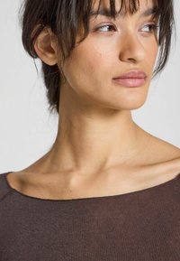 Hnedý, ľahký top s širokým výstrihom a krátkymi rukávmi. Mäkká štruktúra a jemný lesk. Obsahuje jemné švy pozdĺž okrajov.
