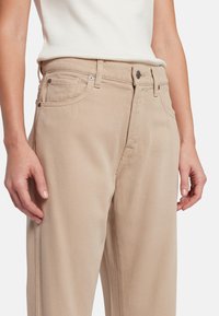 Beige katoenen denim broek met rechte pijpen, voorzien van een knoop- en ritssluiting, vijf zakken en een gestructureerde afwerking.