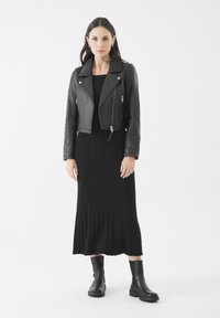 Zwarte leren cropped motorjack over een zwarte geribbelde jurk, gecombineerd met chunky zwarte enkellaarsjes. Gladde textuur en minimale hardware.