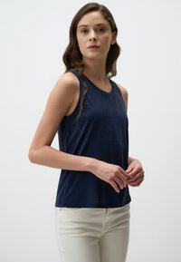 Top senza maniche di colore navy realizzato in tessuto morbido, con scollatura rotonda e una vestibilità rilassata. Abbinato a jeans chiari per un contrasto.
