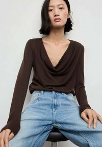 Bruine lange mouwen top met een gedrapeerde halslijn, gecombineerd met lichtblauwe high-waisted jeans. Soepele stof met een relaxte pasvorm.