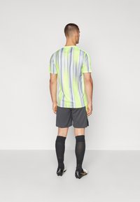 Neon-gelbes und grau gestreiftes Sportshirt, graue Shorts, schwarze knielange Socken und schwarz-weiße Fußballschuhe, von hinten betrachtet.
