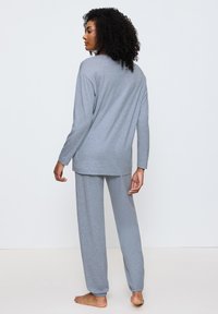 Harmaa loungewear-setti, johon kuuluu pitkähihaisuus paita ja elastisella vyötäröllä varustetut housut, valmistettu pehmeästä kankaasta ja rentoa istuvuutta.
