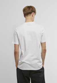 Bíl�ý bavlněný tričko s krátkými rukávy a kulatým výstřihem. Hladká textura, volný střih a jednoduchý design bez dalších vzorů nebo akcentů.