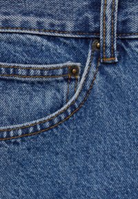 Vaqueros de denim azul que presentan un bolsillo frontal con costuras de contraste, detalles de remaches metálicos y una tela suave y texturizada.