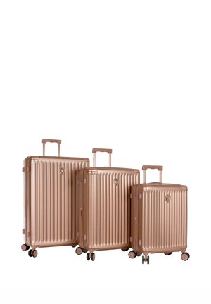 Trois valises rigides en or rose de petites, moyennes et grandes tailles avec des poignées extensibles et quatre roues chacune, disposées côte à côte.