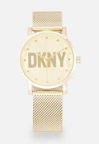 Orologio con cinturino in rete dorata e quadrante rotondo, caratterizzato da grandi lettere "DKNY", marcatori dell'ora minimi a forma di punto e lancette dorate.
