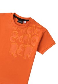 Camiseta de algodón naranja de manga corta, con un diseño gráfico texturizado que dice "Explorador de la Selva" en diferentes tonos de naranja.