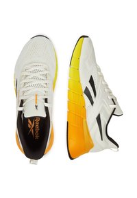 Białe buty sportowe z siateczkową cholewką, czarnymi akcentami oraz grubą, segmentowaną żółto-pomarańczową podeszwą. Sznurówki i logo widoczne na języku.