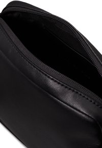 Czarna skórzana torba na zamek błyskawiczny. Gładka tekstura, prosty design i niedopasowane wnętrze. Brak widocznych znaków towarowych lub wzorów.