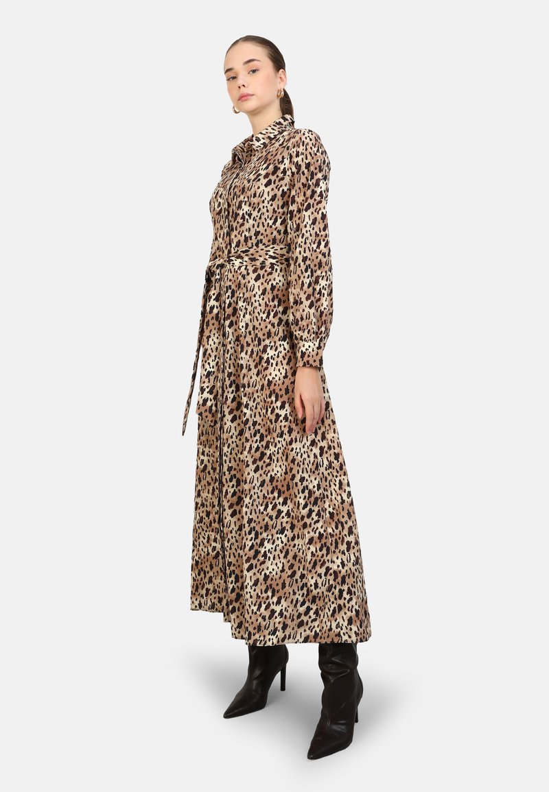 Robe maxi en imprimé léopard beige et marron, avec un col, des manches longues, une taille ceinturée et une jupe fluide. Bottes à talons noires.