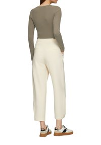 Olijfgroene blouse met lange mouwen, gecombineerd met roomkleurige hoog-geribbelde broeken en witte sneakers met zwarte en gouden accenten.