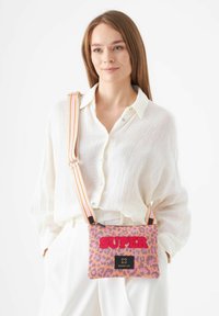 Leopardenmuster Crossbody-Tasche in Pink, mit fettem "SUPER"-Text, Stofftextur und gefärbtem Streifenriemen in zwei Farben. Schwarzes Markenlabel sichtbar.