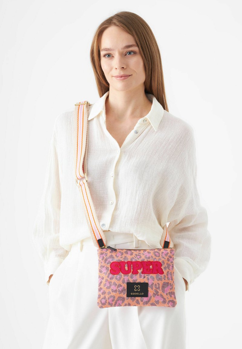 Leopardenmuster Crossbody-Tasche in Pink, mit fettem "SUPER"-Text, Stofftextur und gefärbtem Streifenriemen in zwei Farben. Schwarzes Markenlabel sichtbar.