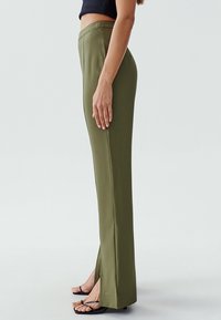 Olivgrüne Hose mit schmalem Schnitt, hoher Taille und seitlichen Schlitzen am Saum. Glatter Stoff mit klaren Linien und ohne sichtbare Muster.