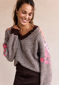 Maglione a righe marrone e crema con scollatura a V. Presenta ricami floreali rosa sulle maniche. Texture morbida, vestibilità comoda e polsini a coste.