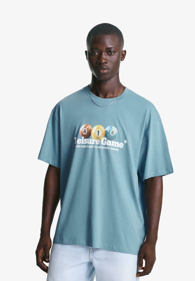 Svijetloplavi oversized majica od pamuka s okruglim izrezom, na kojoj su tiskane grafike kuglica za bazen i natpis "Leisure Game."