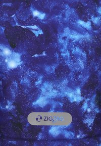 Sininen kangas, jossa on tähtiä esittävä avaruuskuvio, joka sisältää vaihtelevaa sinisen sävyä ja valkoisia täpliä, alalaidassa harmaa "ZIGZAG" -logo.