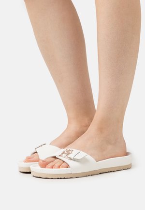 Witte slides met een glad bovenwerk, voorzien van een metalen accent. De zool is beige met een textuur voor grip en stabiliteit.